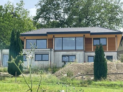 Vue d'ensemble d'une maison contemporaine en bois et aluminium à Montagnole, implantée sur un terrain en pente avec soubassement en béton