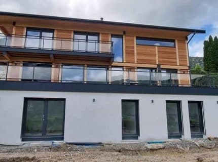 Maison en bois contemporaine de 180 m² à Lathuile en Haute-Savoie, avec bardage bois, grandes baies vitrées et soubassement crépi.