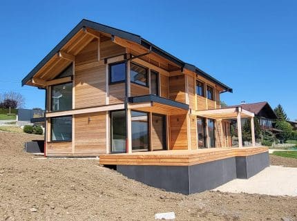 Maison à ossature bois de deux niveaux à Reignier-Ésery en Haute-Savoie, avec bardage en bois naturel, toit deux pans et sous-bassement en béton.