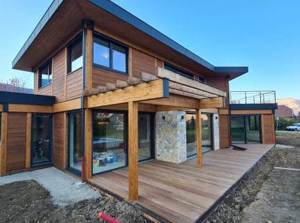 Maison en bois poteau-poutre avec bardage bois, aluminium et terrasse en bois, située à Saint-Jorioz près du lac d’Annecy.