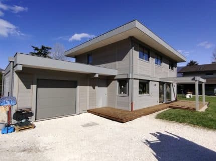 Façade d’une maison contemporaine à ossature bois et finitions aluminium à St Jorioz, avec bardage bois grisé et terrasse en bois