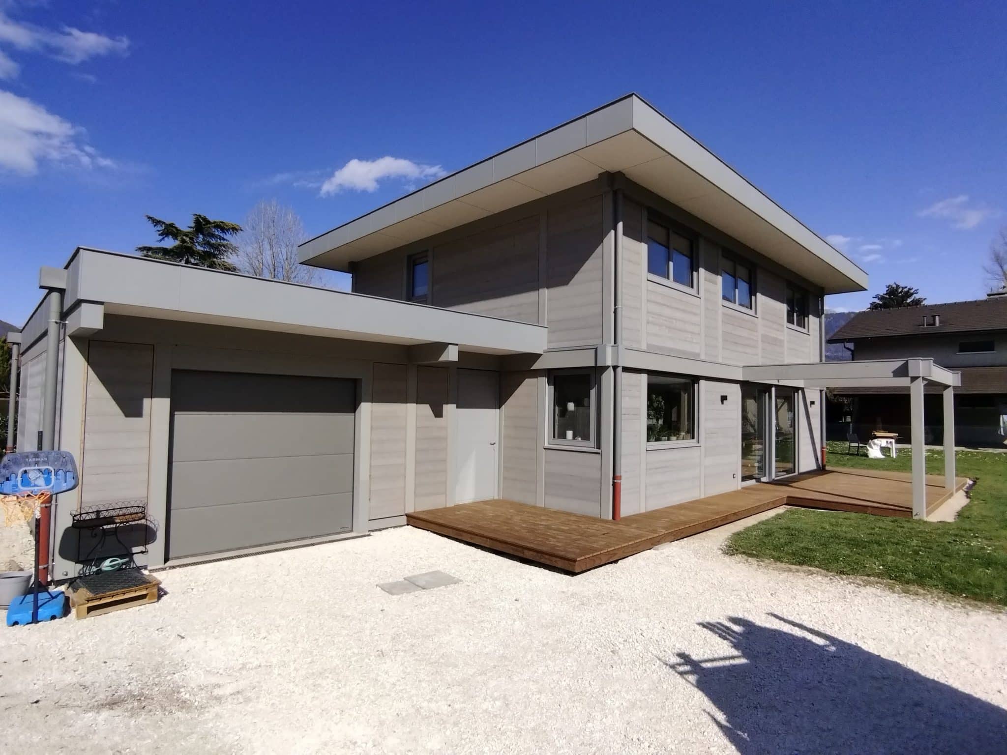 Façade d’une maison contemporaine à ossature bois et finitions aluminium à St Jorioz, avec bardage bois grisé et terrasse en bois
